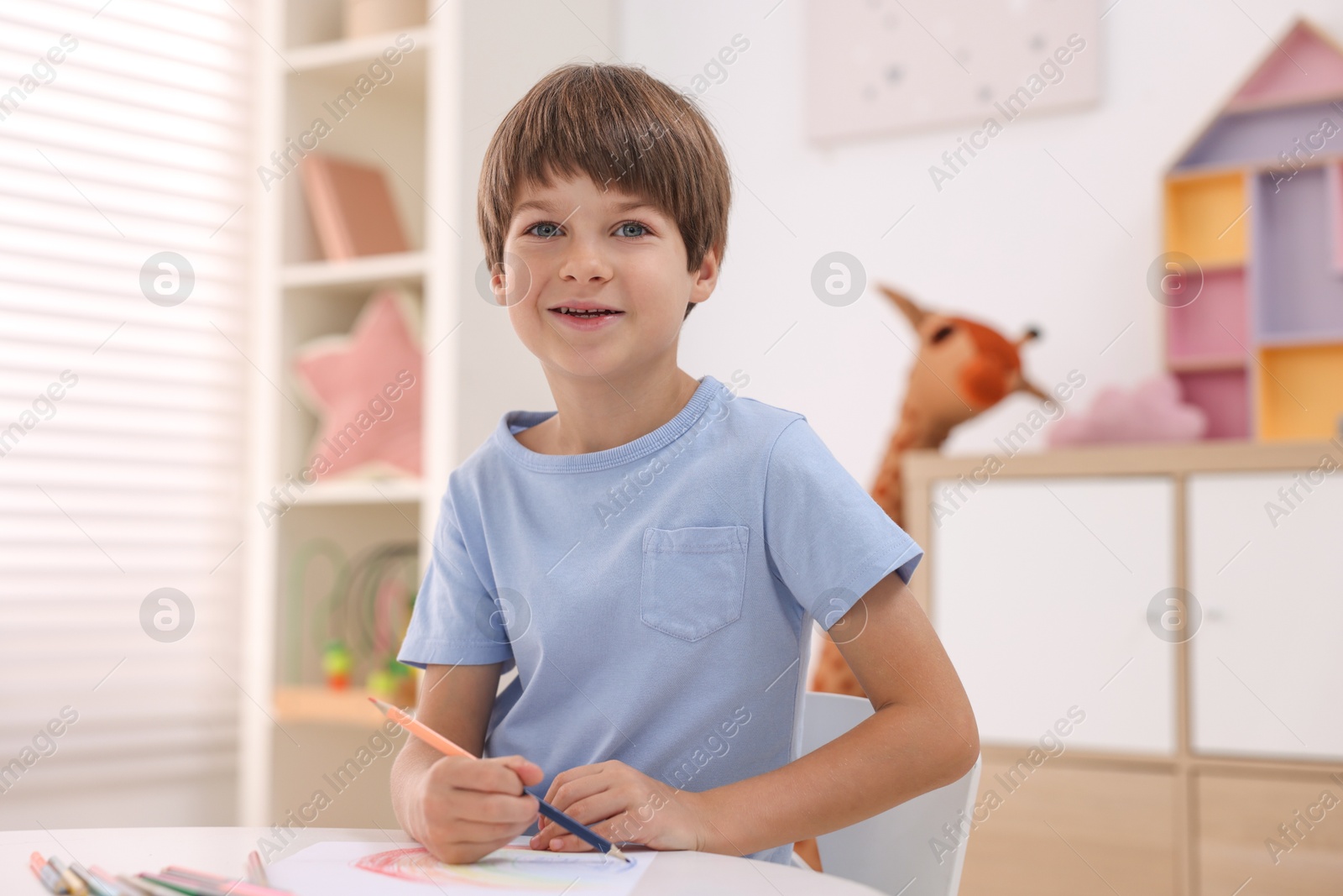 Photo of Smiling boy drawing at table in kindergarten