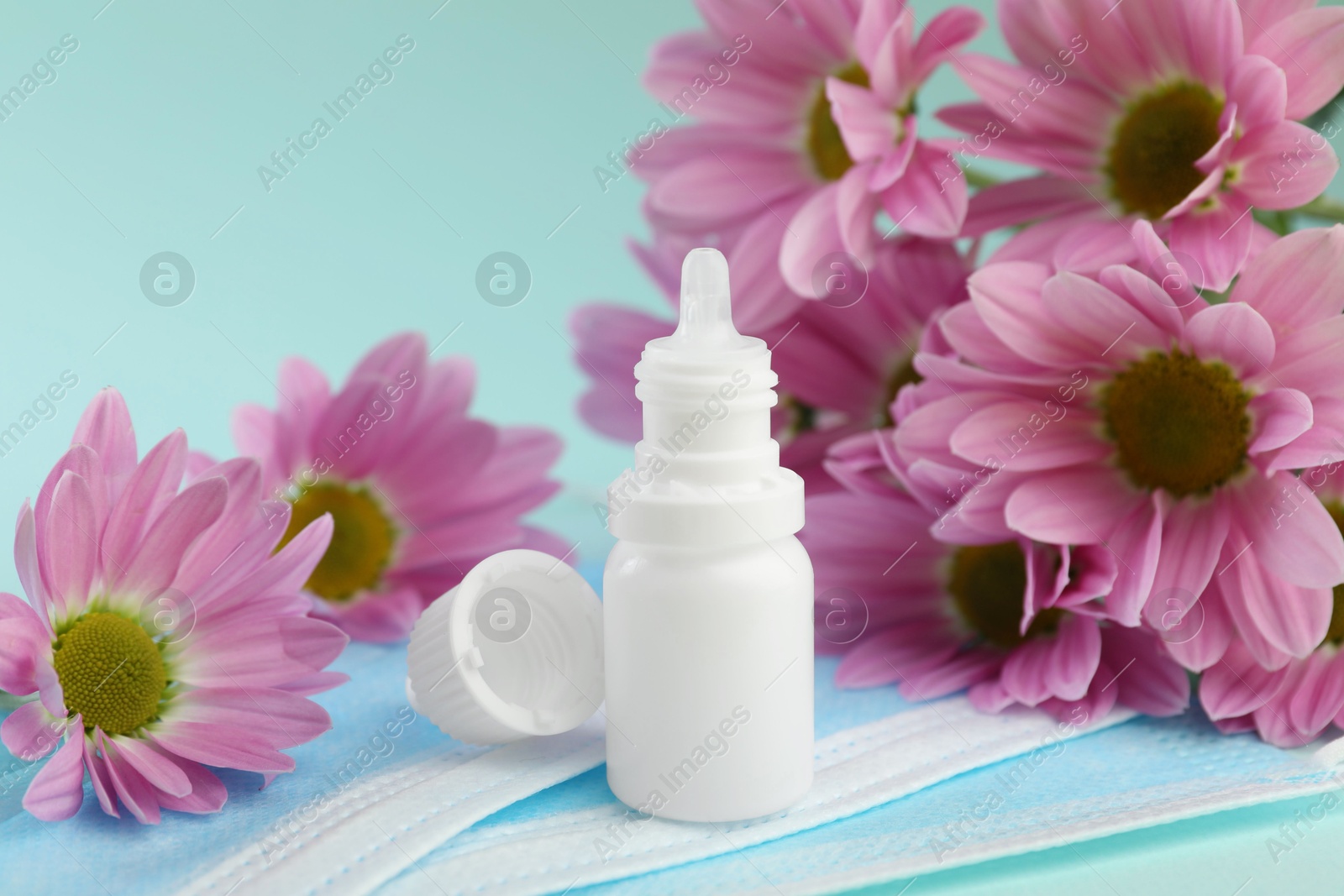 Photo of Allergy treatment. Nasal drops, protective masks and flowers on light blue background, closeup