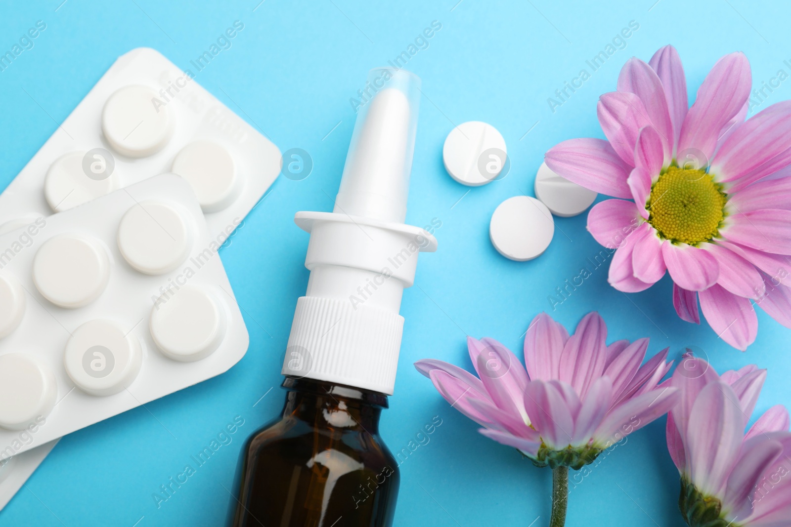 Photo of Allergy treatment. Nasal spray, pills and flowers on light blue background, flat lay