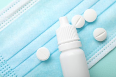 Photo of Allergy treatment. Nasal drops, pills and protective mask on light blue background, closeup