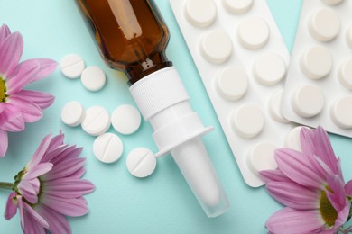 Photo of Allergy treatment. Nasal spray, pills and flowers on light blue background, flat lay