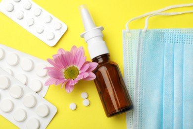 Photo of Allergy treatment. Nasal spray, pills, protective masks and flower on yellow background, flat lay