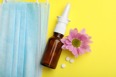 Photo of Allergy treatment. Nasal spray, pills, protective masks and flower on yellow background, flat lay