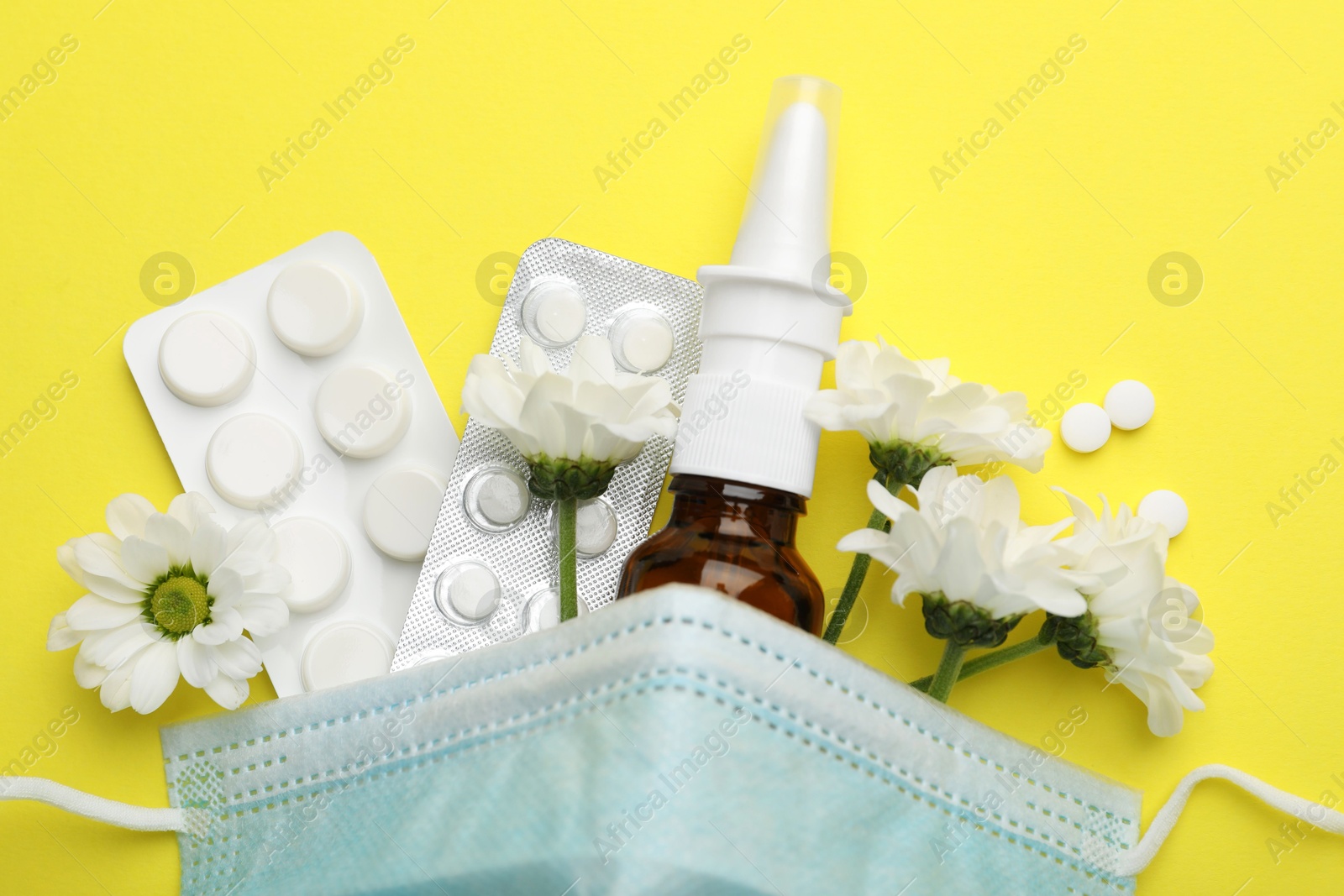 Photo of Allergy treatment. Nasal spray, pills, protective mask and flowers on yellow background, flat lay