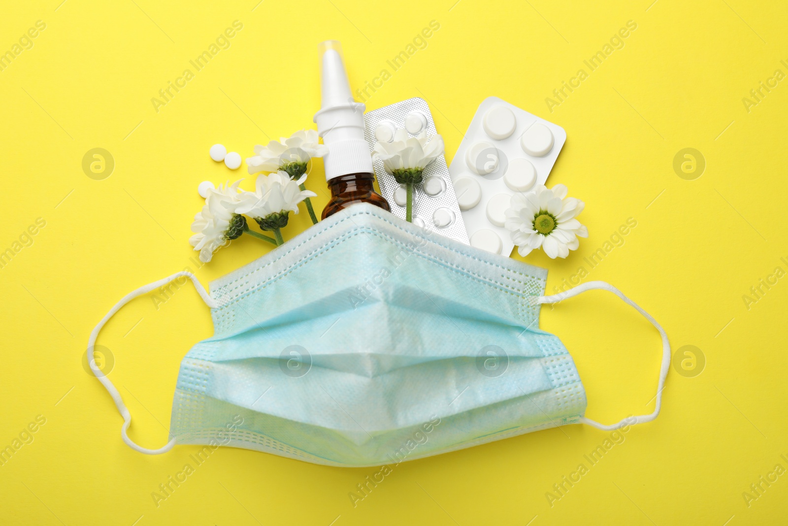 Photo of Allergy treatment. Nasal spray, pills, protective mask and flowers on yellow background, flat lay