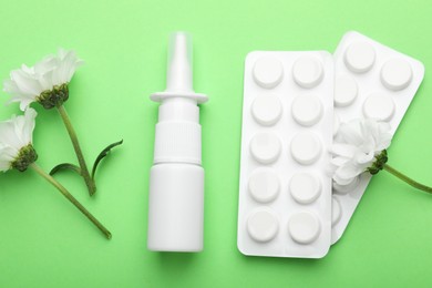 Photo of Allergy treatment. Nasal spray, pills and flowers on green background, flat lay