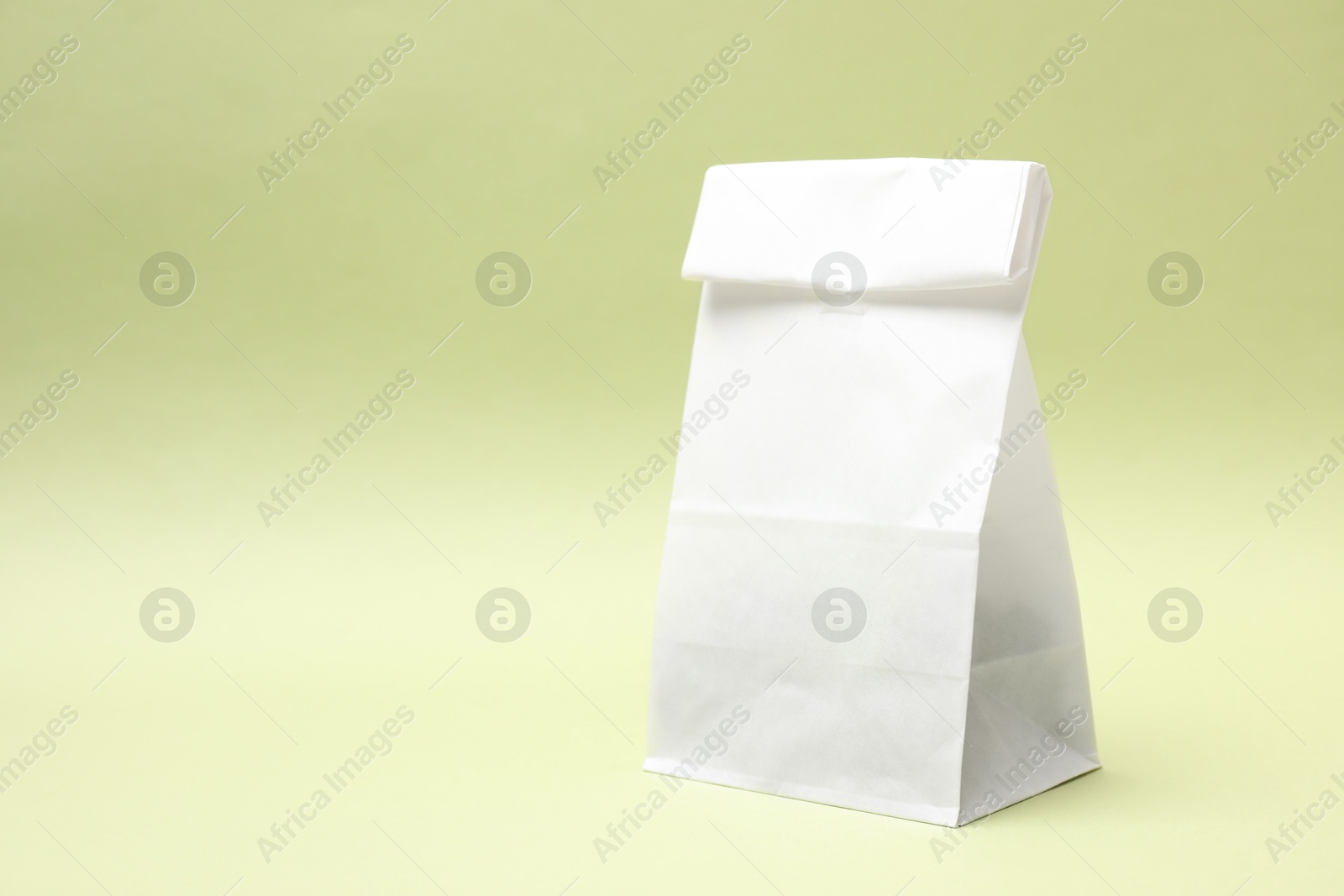 Photo of One closed paper bag on light green background. Space for text