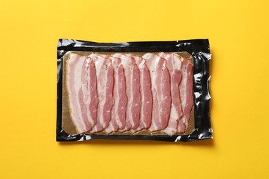 Photo of Pack of bacon on yellow background, top view