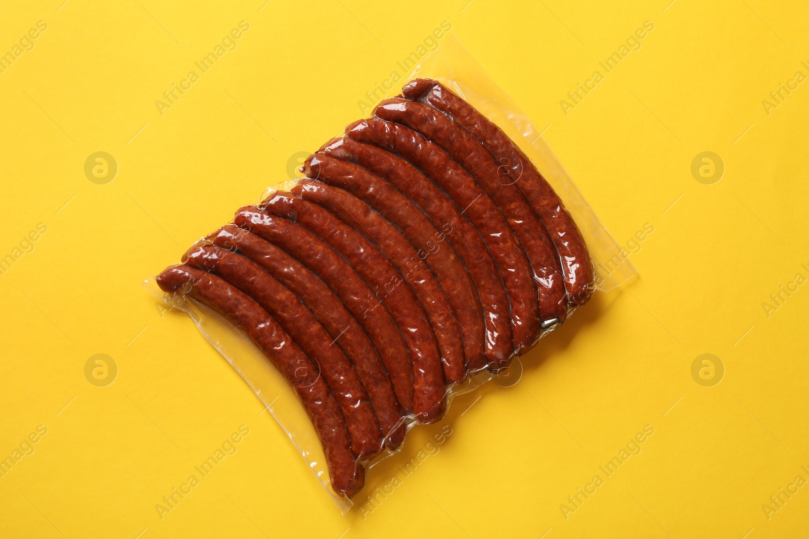 Photo of Pack of smoked sausages on yellow background, top view