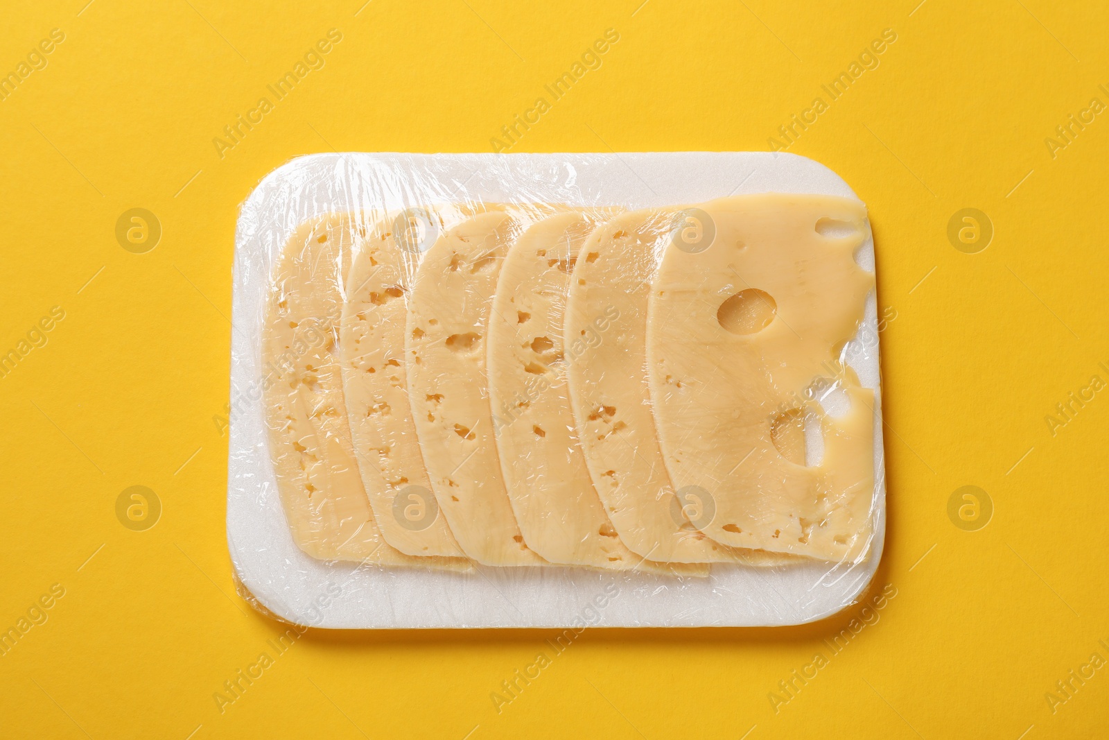 Photo of Pack of sliced cheese on yellow background, top view