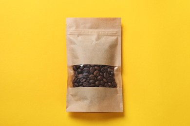 Photo of Paper pouch bag with coffee beans on yellow background, top view