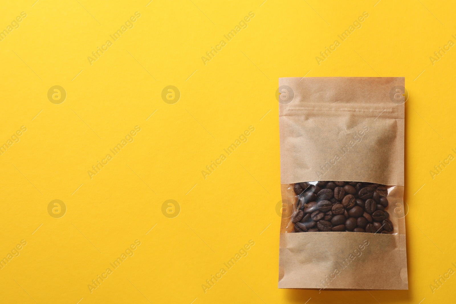 Photo of Paper pouch bag with coffee beans on yellow background, top view. Space for text