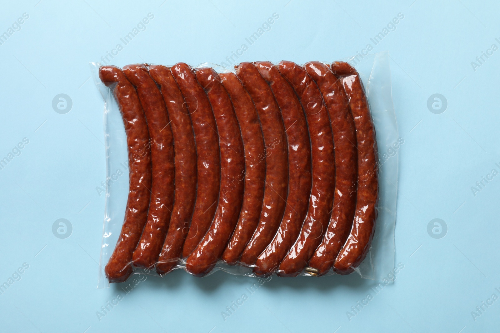 Photo of Pack of smoked sausages on light blue background, top view