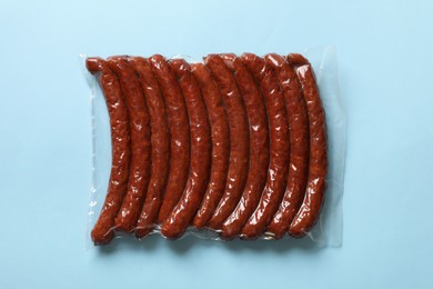 Photo of Pack of smoked sausages on light blue background, top view