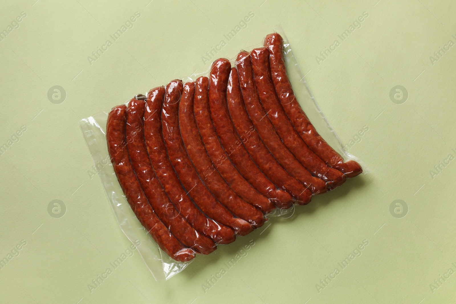 Photo of Pack of smoked sausages on green background, top view