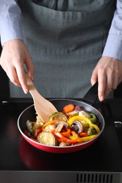 Photo of Woman frying vegetables and mushrooms in pan on stove, closeup