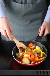 Photo of Woman frying vegetables and mushrooms in pan on stove, closeup