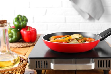 Photo of Frying pan with vegetables, stove and oil on wooden table indoors, closeup