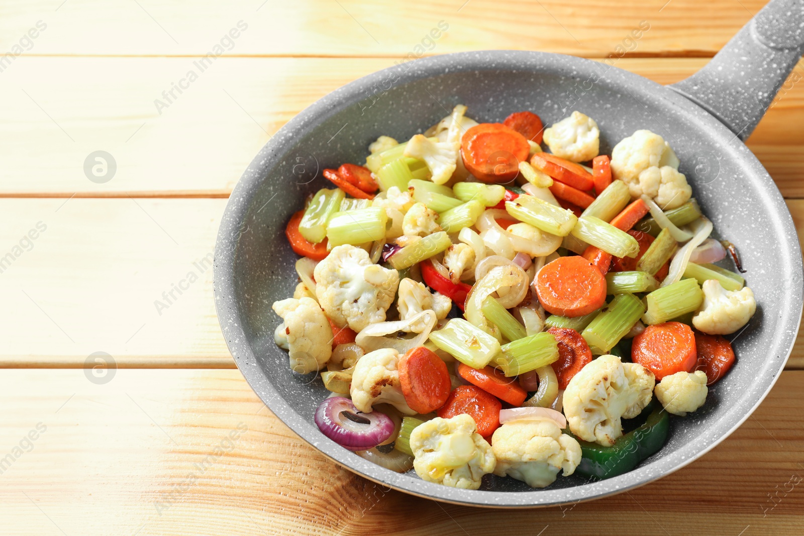 Photo of Frying pan with vegetables on wooden table, closeup. Space for text