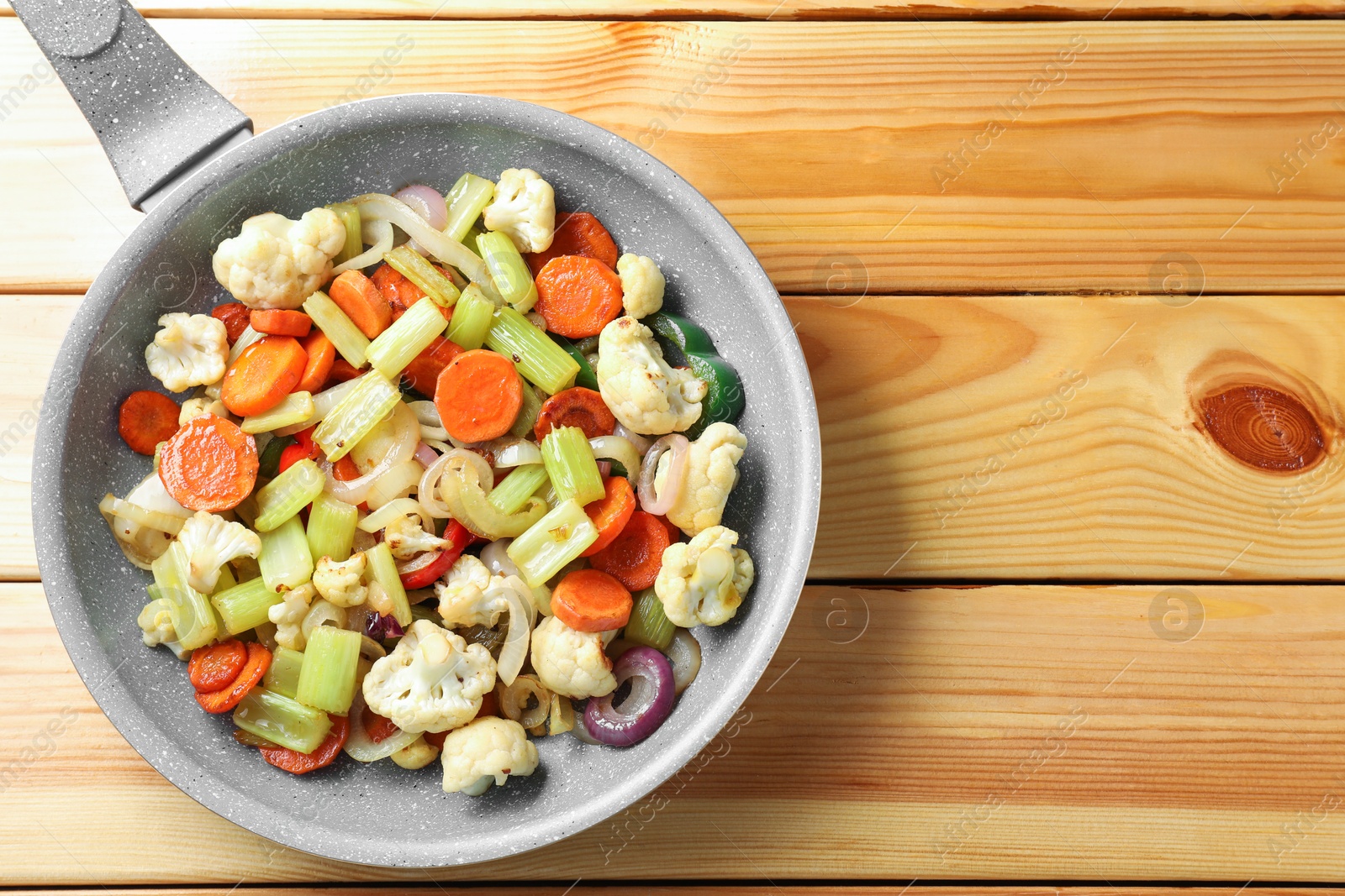 Photo of Frying pan with vegetables on wooden table, top view. Space for text