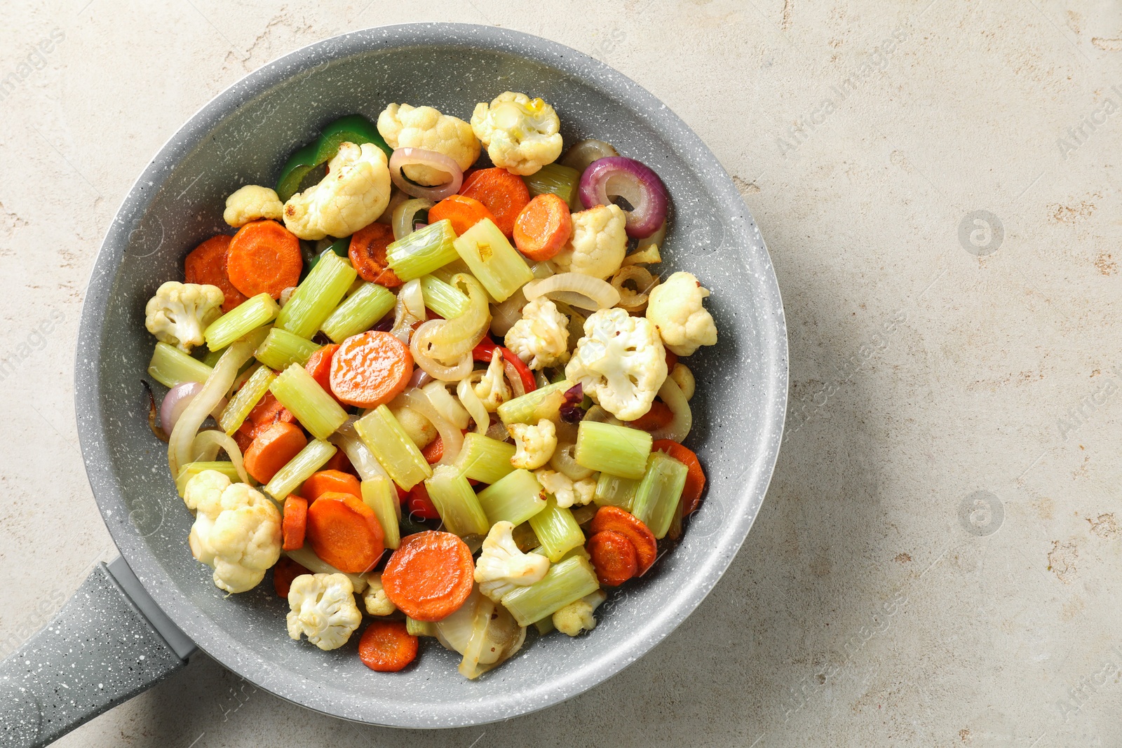 Photo of Frying pan with vegetables on light textured table, top view. Space for text