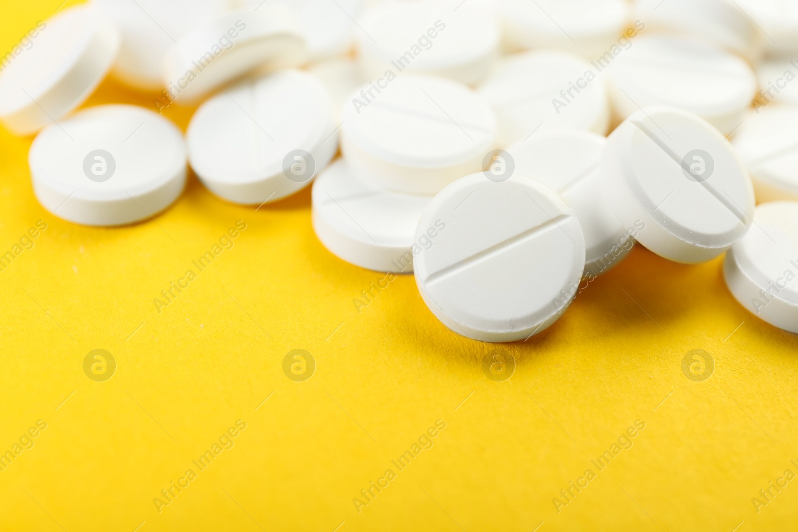 Photo of Pile of antibiotic pills on yellow background, closeup