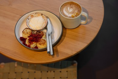 Photo of Delicious cottage cheese pancakes and tasty latte served on wooden table in cafe, closeup