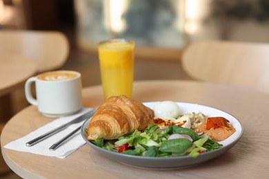 Photo of Tasty breakfast. Freshly baked croissant and salad served on wooden table in cafe, closeup