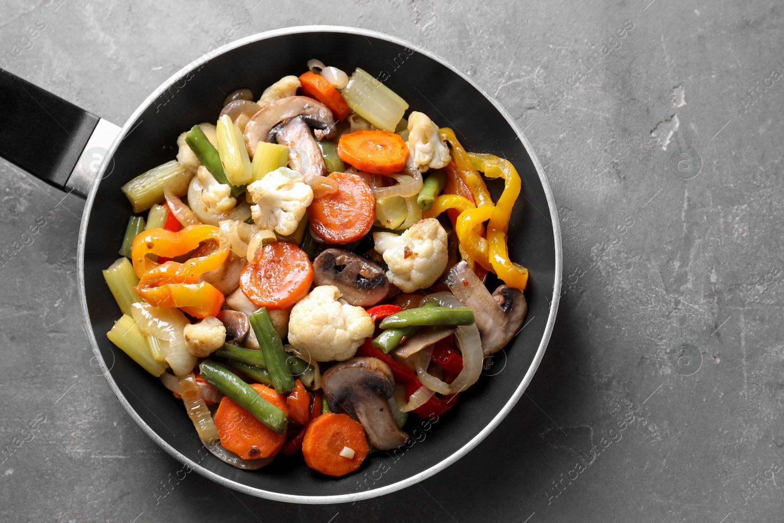 Photo of Different vegetables and mushrooms in frying pan on grey table, top view