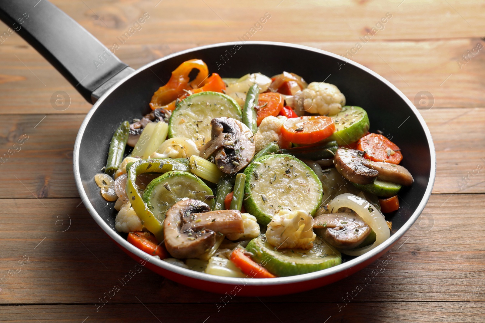 Photo of Different vegetables and mushrooms in frying pan on wooden table, closeup