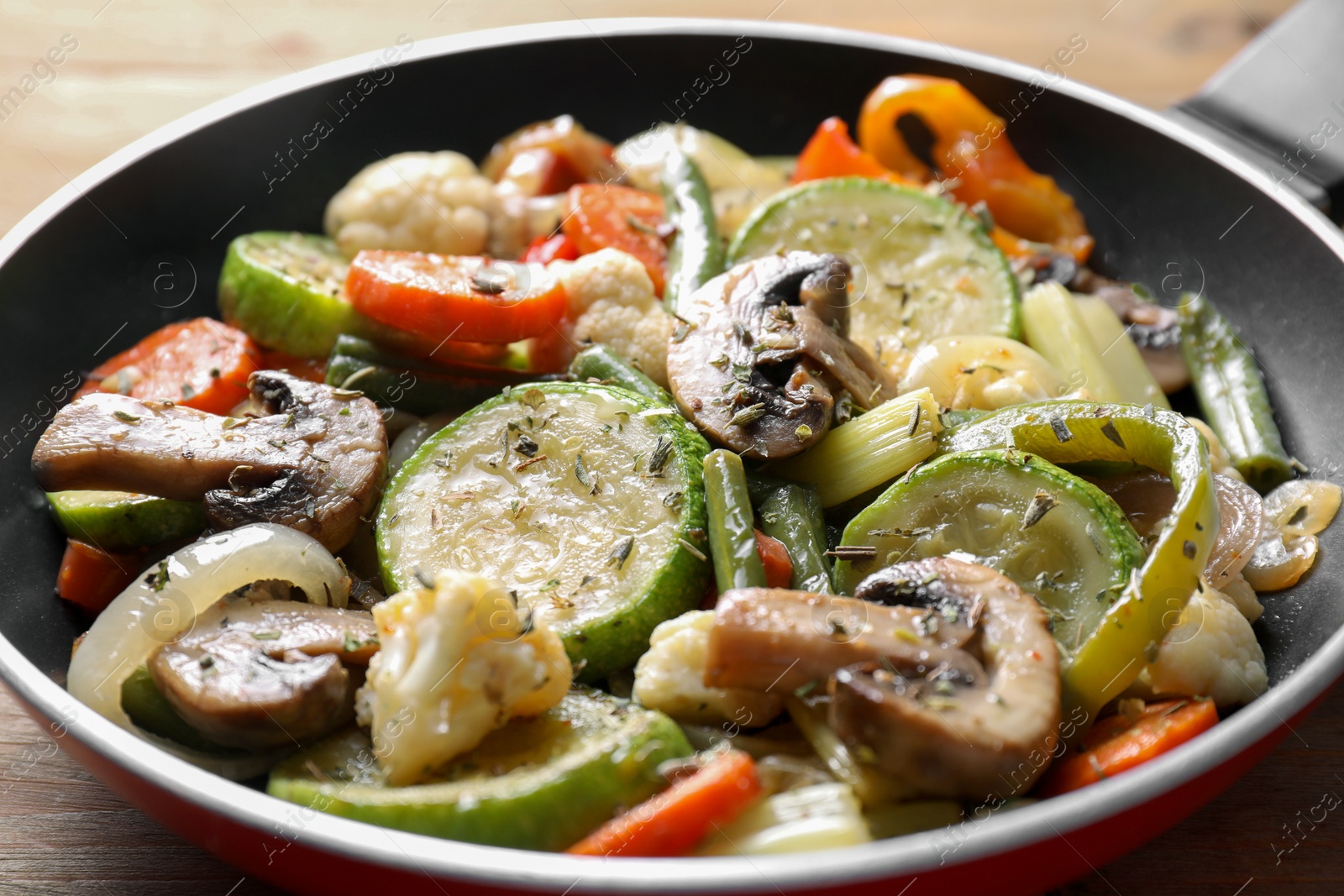 Photo of Different vegetables and mushrooms in frying pan on wooden table, closeup