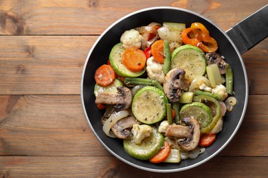 Photo of Different vegetables and mushrooms in frying pan on wooden table, top view