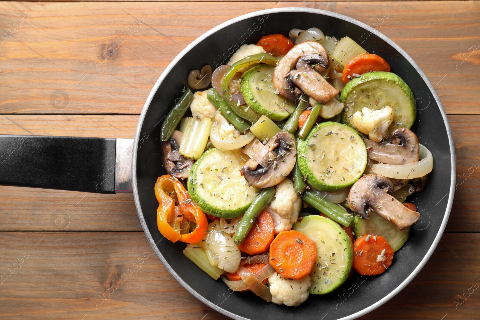 Photo of Different vegetables and mushrooms in frying pan on wooden table, top view