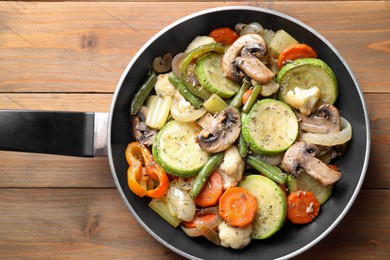 Different vegetables and mushrooms in frying pan on wooden table, top view