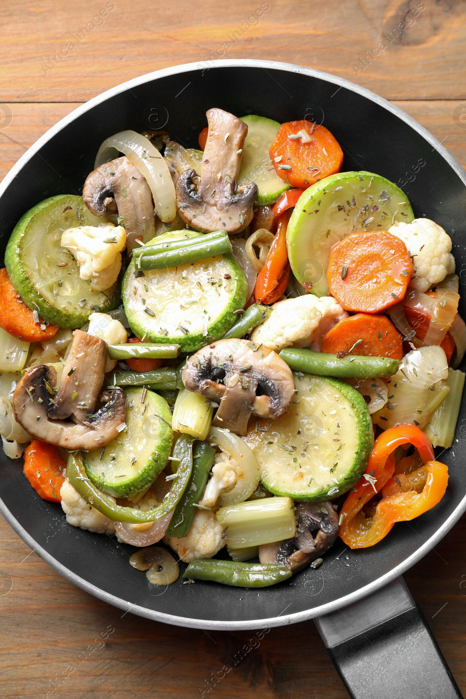 Photo of Different vegetables and mushrooms in frying pan on wooden table, top view