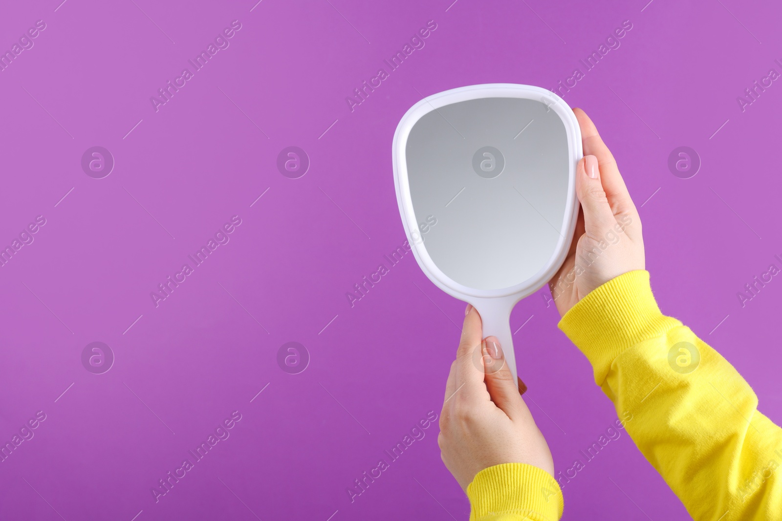 Photo of Woman holding handheld mirror on violet background, closeup. Space for text