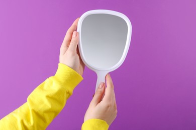 Photo of Woman holding handheld mirror on violet background, closeup