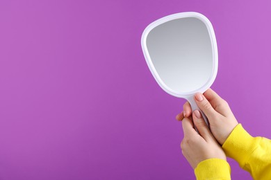 Photo of Woman holding handheld mirror on violet background, closeup. Space for text