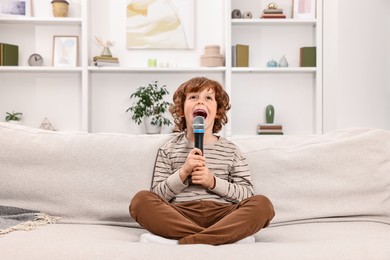 Photo of Little boy with microphone singing on sofa at home