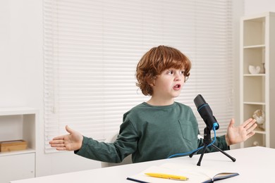 Photo of Little boy with microphone at white table indoors