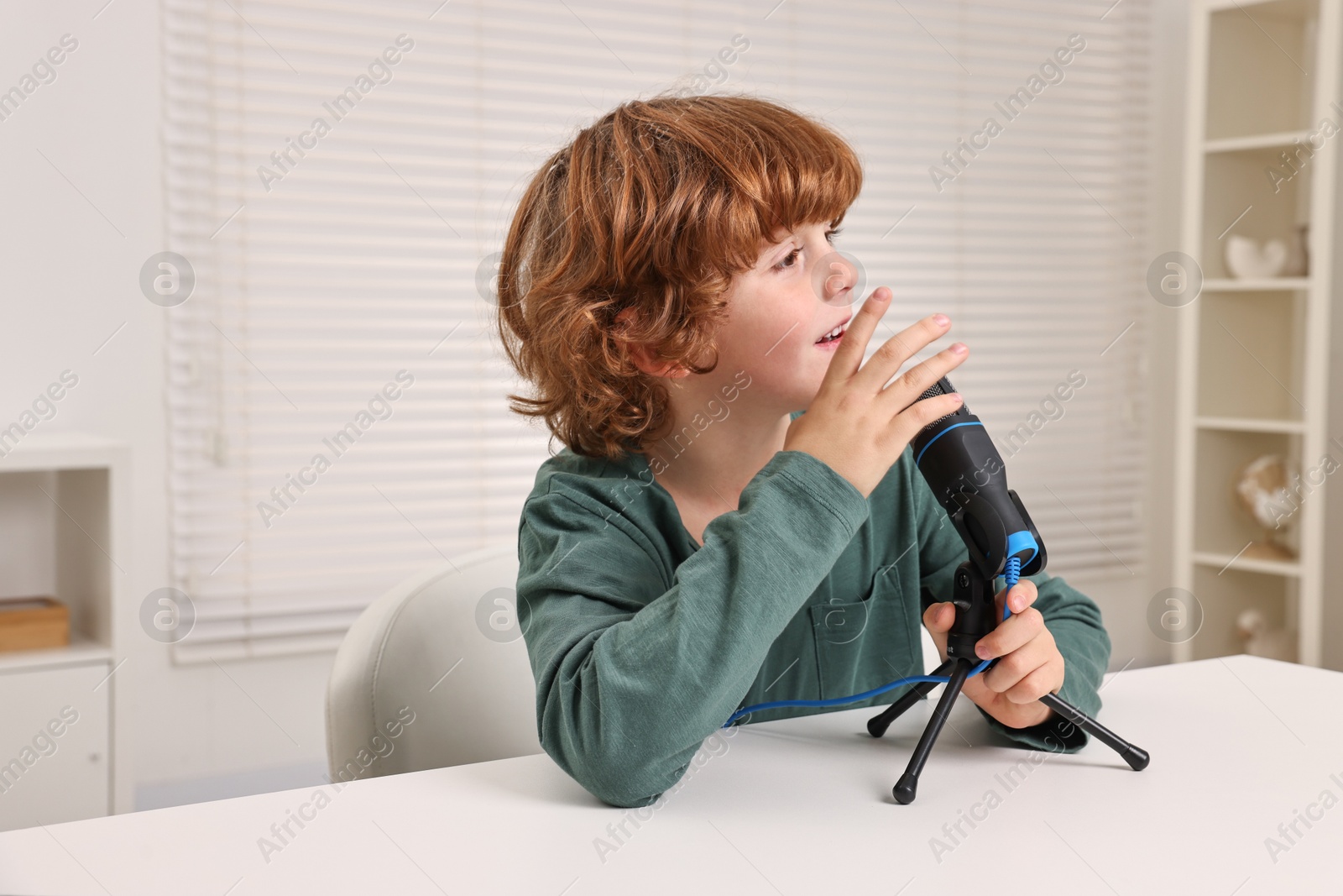 Photo of Little boy with microphone at white table indoors