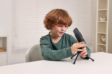 Photo of Little boy with microphone at white table indoors