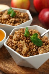 Photo of Tasty apple crisp in bowls, fresh fruits, honey and spoon on table, closeup