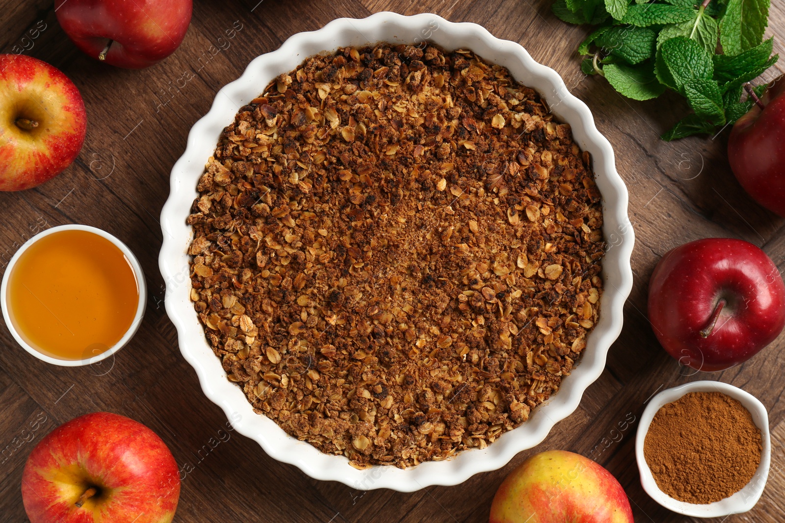 Photo of Tasty apple crisp in baking dish and ingredients on wooden table, flat lay