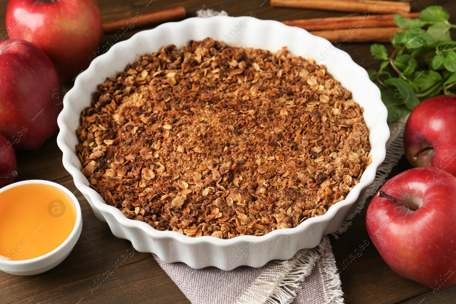 Photo of Tasty apple crisp in baking dish and ingredients on wooden table, closeup