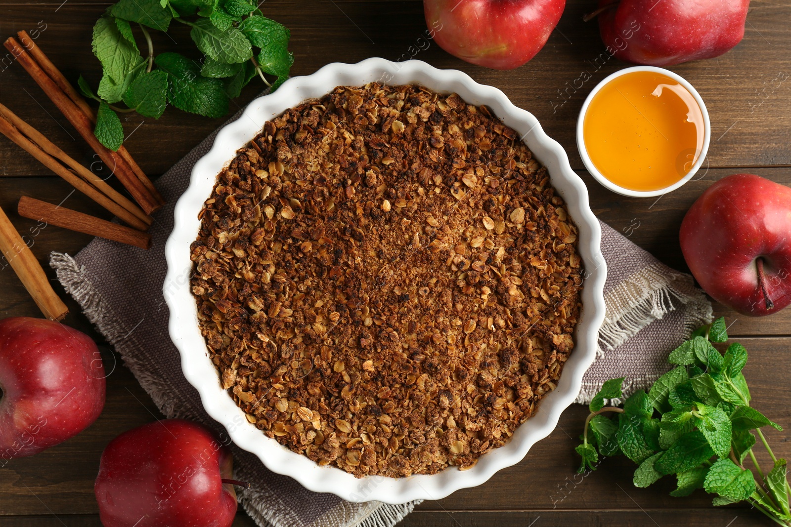 Photo of Tasty apple crisp in baking dish and ingredients on wooden table, flat lay