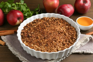 Photo of Tasty apple crisp in baking dish and ingredients on wooden table, closeup