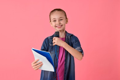 Photo of Little girl with microphone and notebook on pink background