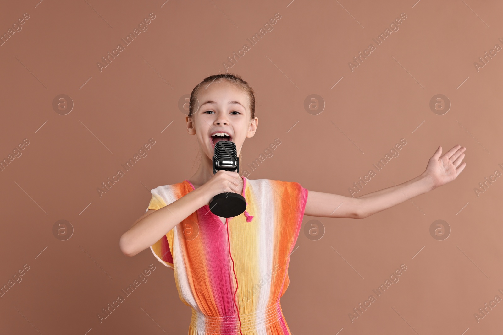 Photo of Little girl with microphone singing on light brown background