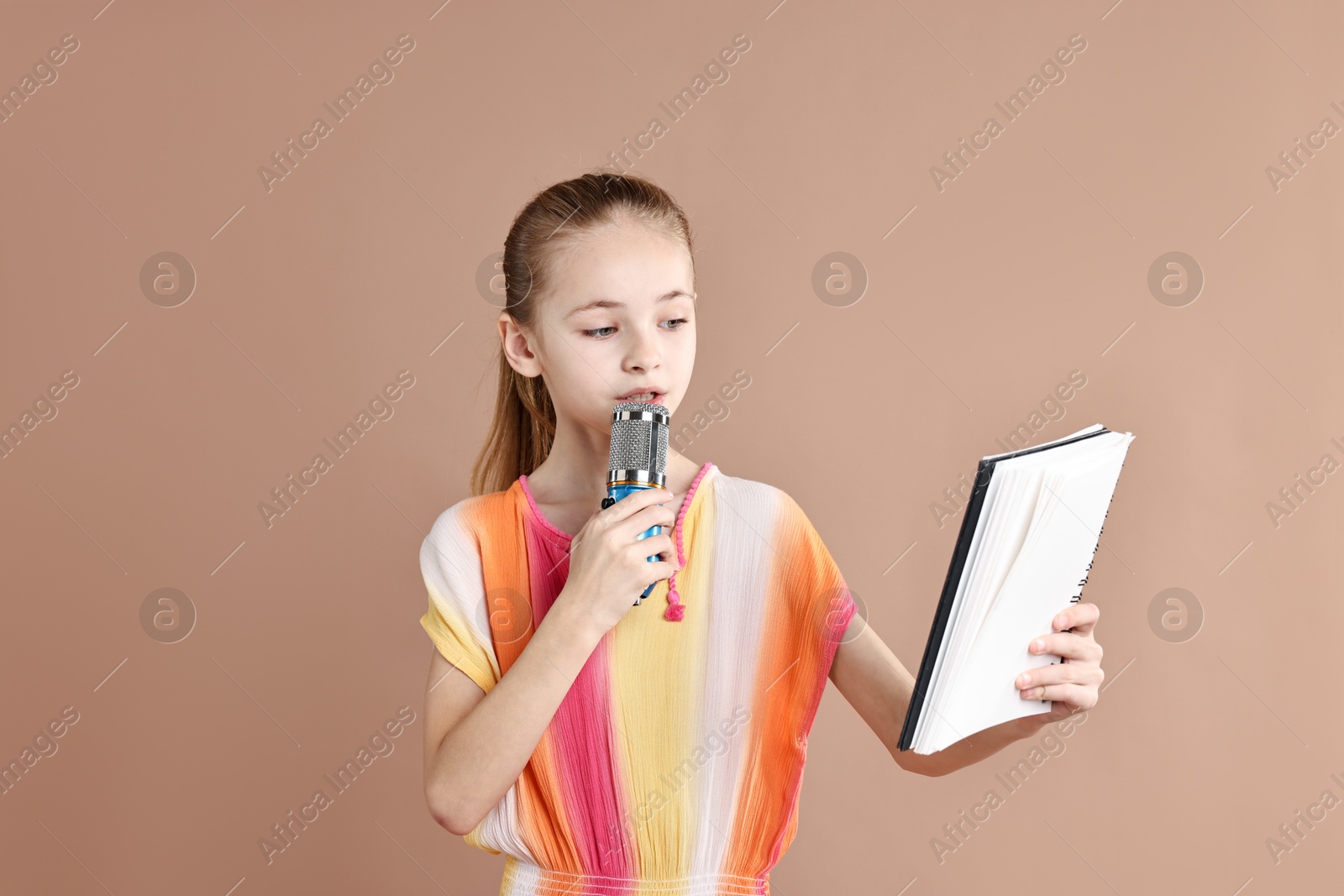 Photo of Little girl with microphone and notebook on light brown background